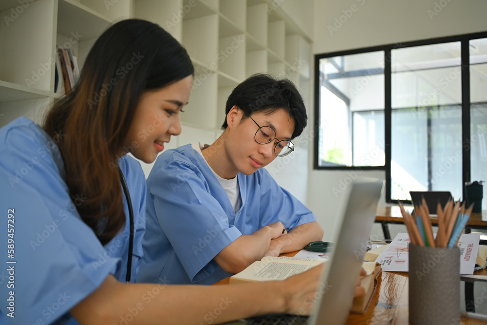 Two male and female medical students talking and using laptop during the lesson in the classroom Two male and female medical students talking and using laptop during the lesson in the classroom