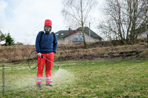 Farmer spraying pesticide on lawn field wearing protective clothing. Treatment of grass from weeds and dandelion. Pest control. Insecticide sprayer with a proper protection. Gardening care season © Hanna