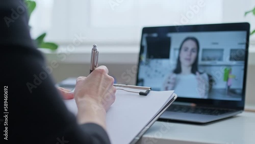 Talking young woman on laptop screen and female with clipboard making notes, video chat