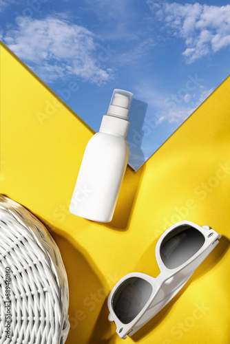 Top view of sunglasses, sunblock, SPF cream, sky mirrow on a yellow table. Concept of beach accessories and holiday.