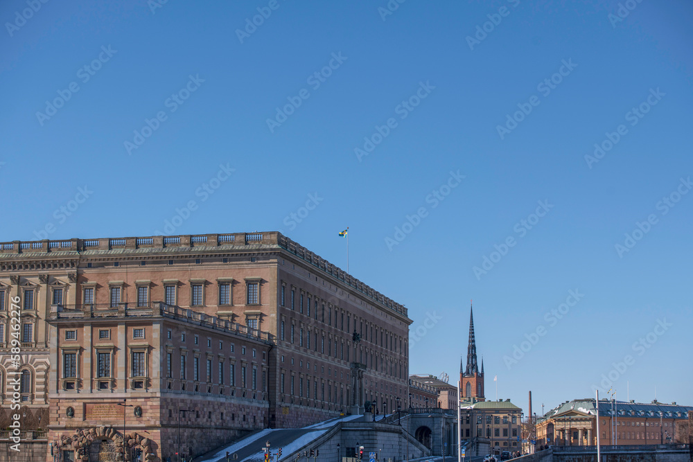 Facades of the royal castle and roof with the royal Swedish flag, the government house and a church tower, a sunny spring day in Stockholm