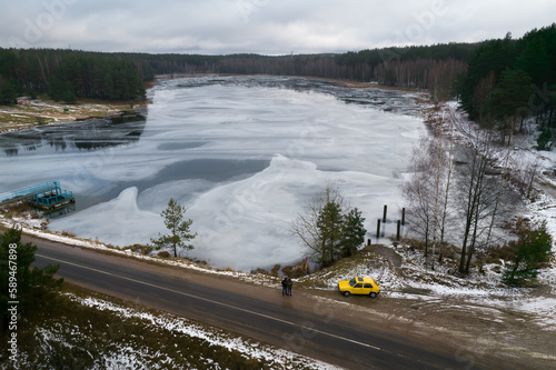 Top view of the frozen spruce forest lake two man stand near yellow retro auto