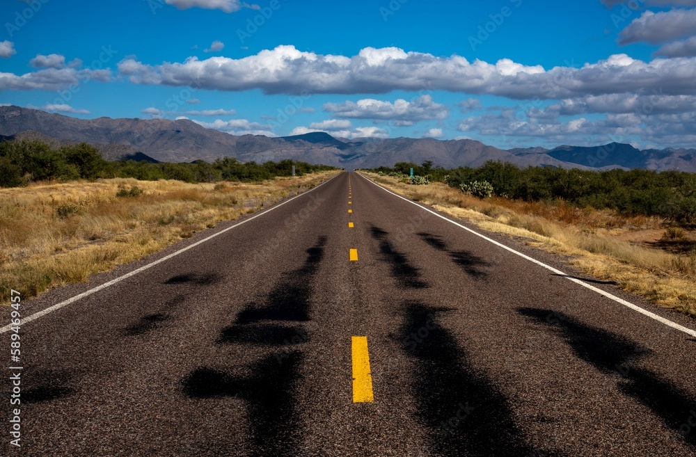 Long empty road in the middle of a desert with mountains in the background