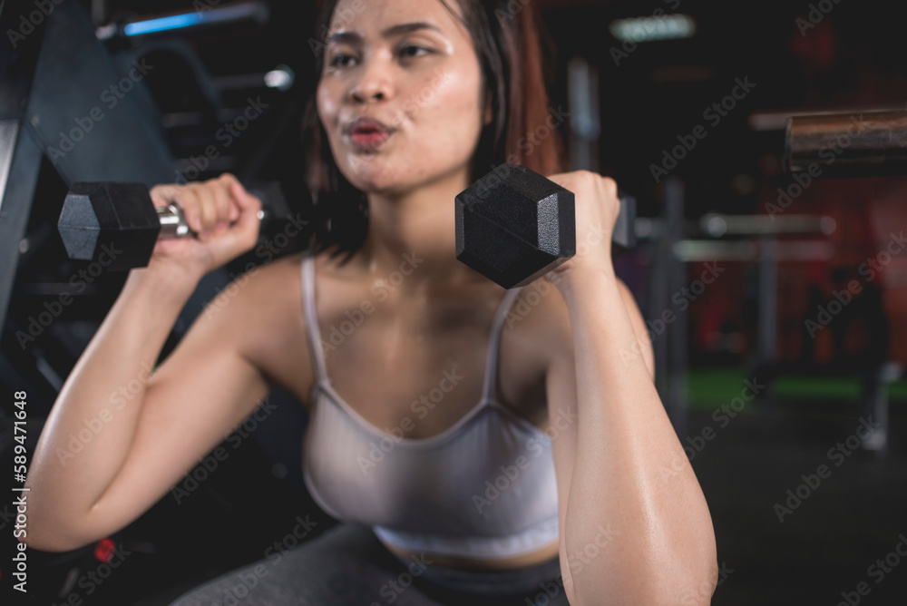 A fit young asian woman does dumbbell squats, holding the dumbbells in the front rack position. Training legs at a modern gym. A fit young asian woman does dumbbell squats, holding the dumbbells in the front rack position. Training legs at a modern gym.