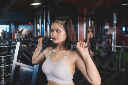 A serious young woman does a set of standing dumbbell presses. Training and toning shoulder muscles at the gym.