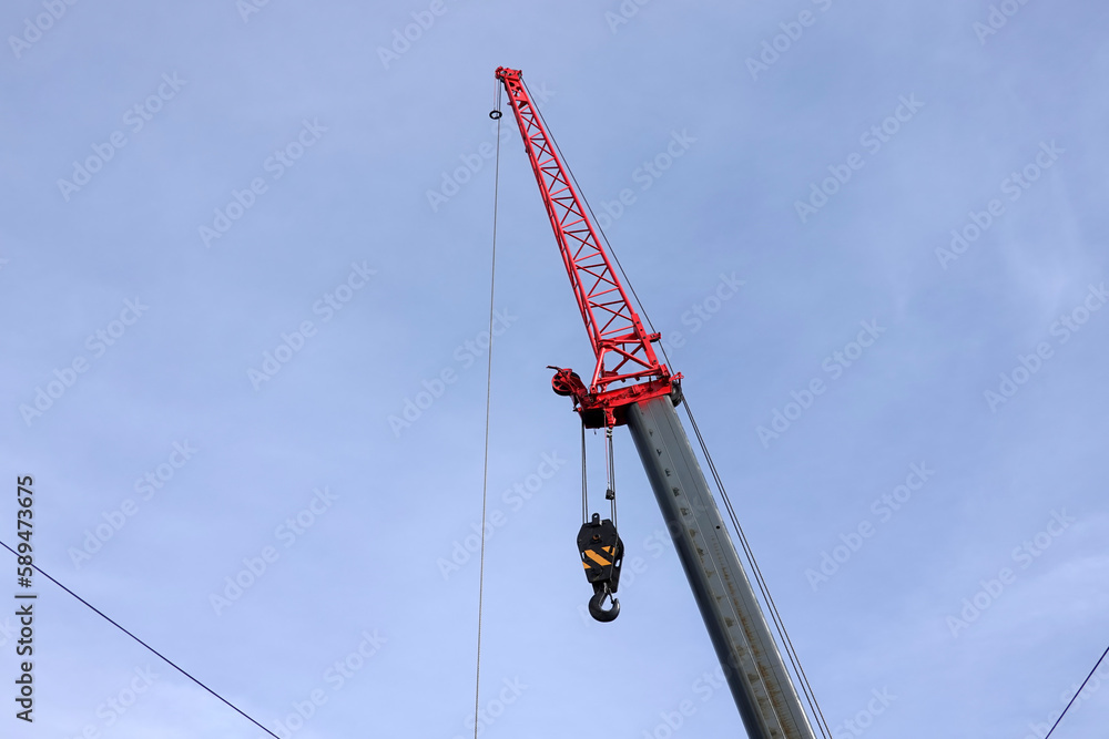 Big construction arm crane with heavy hook on metal cable on clear blue sky