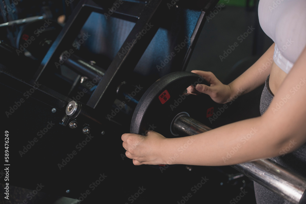 Naklejka premium A young anonymous woman loading plates for more weight on a leg press machine at the gym.