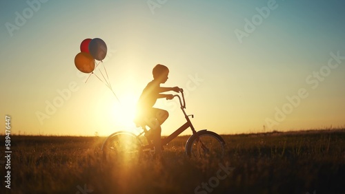 child learns to ride a bike in the park silhouette. happy family kid dream concept. son child travels by bike. kid dream of moving fast on a bike. silhouette boy rides a bike with balloons lifestyle
