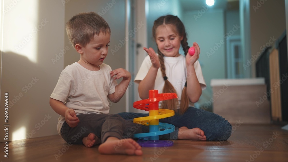 Fototapeta premium children baby play together toys in kindergarten. happy family preschool education indoor concept. baby boy and girl play toy roll a ball down a slide on lifestyle the floor rejoice in kindergarten