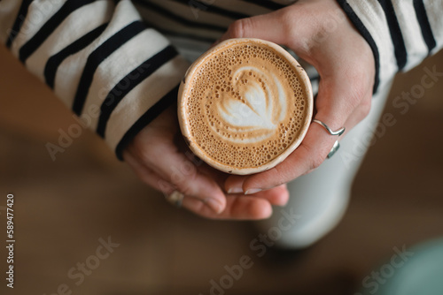 Top view of woman in striped longsleeve holding ceramic cup of cappuccino. 