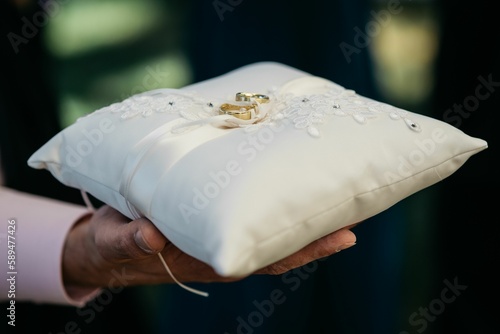 Photos Person holding a white pillow with wedding rings on it.