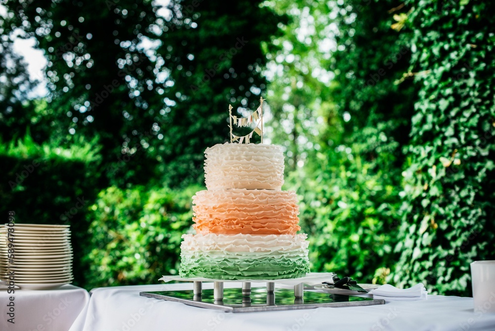Beautiful orange three tiered cake on a table with trees in the background