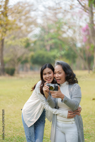 Asian teenage mother and daughter walking in park with camera to capture memories