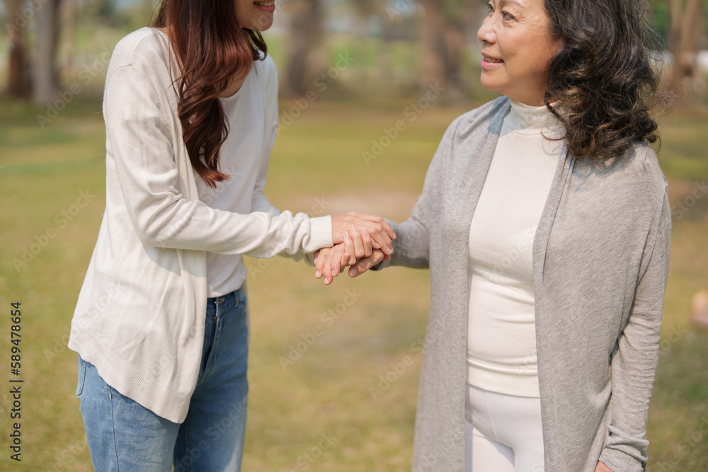 Adult daughter holding her elderly mother hand with love and walk together in park Adult daughter holding her elderly mother hand with love and walk together in park