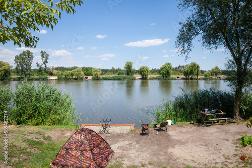 Fhsing rod and tent in front of a Panorama of Lake Jezero Tresetiste in summer, during a sunny afternoon. Tresetiste is a fishing pond lake in Subotica, near suboticka pescara, in Serbia, vojvodina.