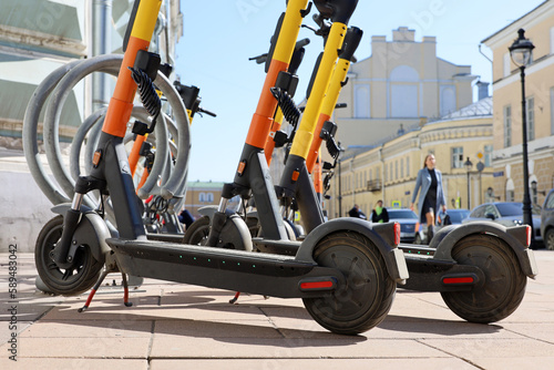 Electric scooters in a row on the parking lot on city buildings and walking people background. Rental system, public e-scooters on the street