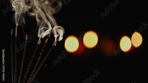 A closeup of burning incense sticks with smoke over a black blur background