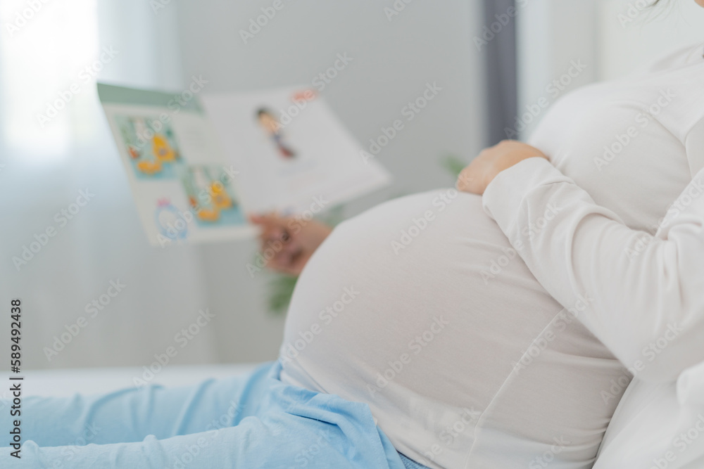 Pregnant woman is reading a story book to her baby. Reading to your