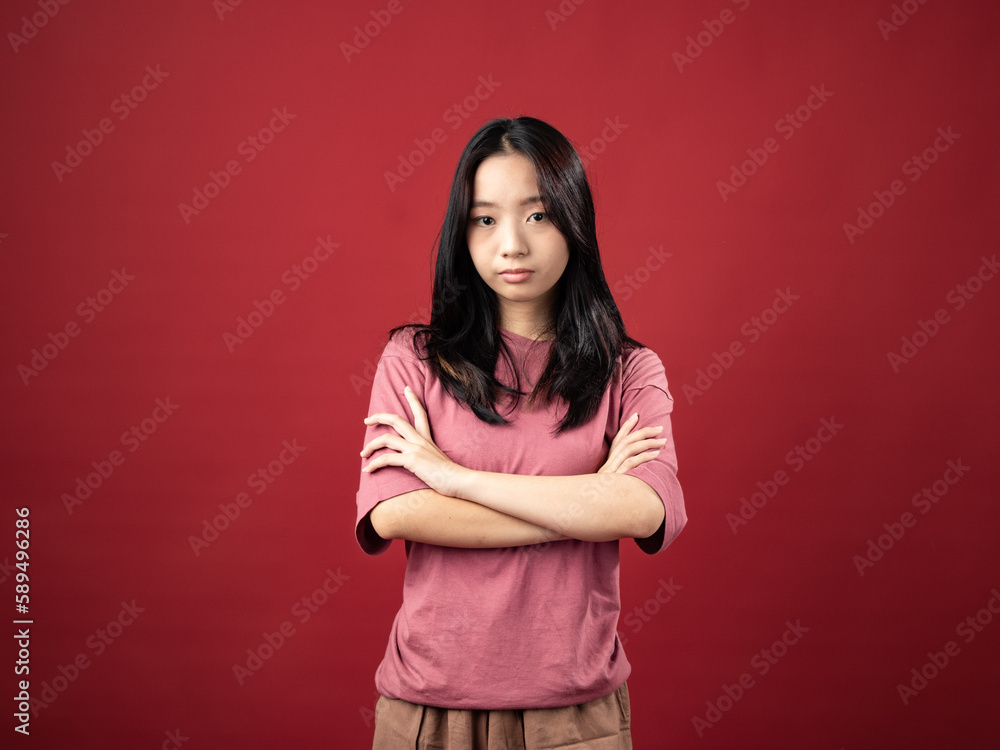 Obraz premium A portrait of a young Indonesian (Asian) woman wearing a pink shirt, posing with folded hands. Isolated with a red background