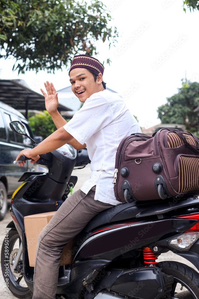 Naklejka premium Smiling young muslim man waving hand saying goodbye to travel mudik at eid mubarak moment 