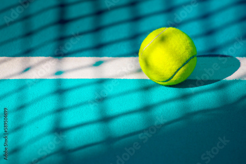 close-up of a tennis ball lying on a hard blue court in the shadow of a tennis net