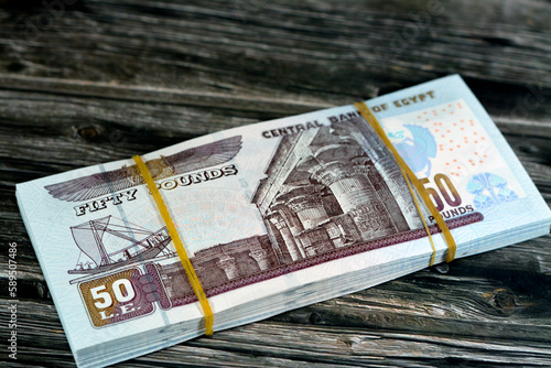 Egypt money stack of pounds isolated on wood background, pile of 50 EGP LE fifty Egyptian pounds cash money bills with a image of Abu Hurayba Mosque, temple of Edfu and winged scarab, selective focus photo