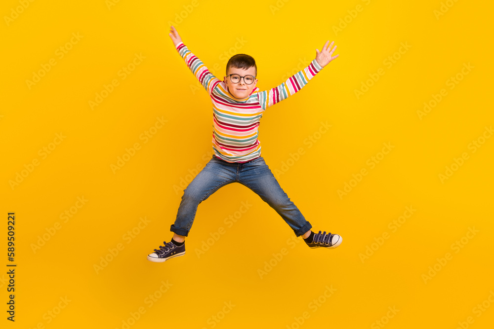 Full length photo of active kid boy jumping up raising hands isolated on vibrant color background