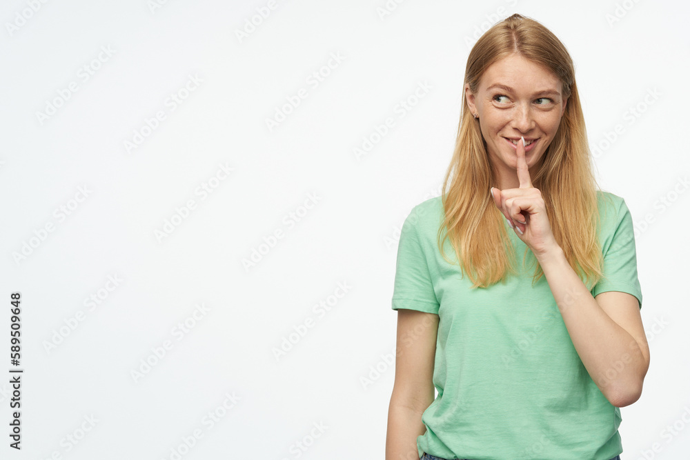 Indoor studio portrait of young ginger female with freckles shows silence gesture isolated over background Indoor studio portrait of young ginger female with freckles shows silence gesture isolated over background