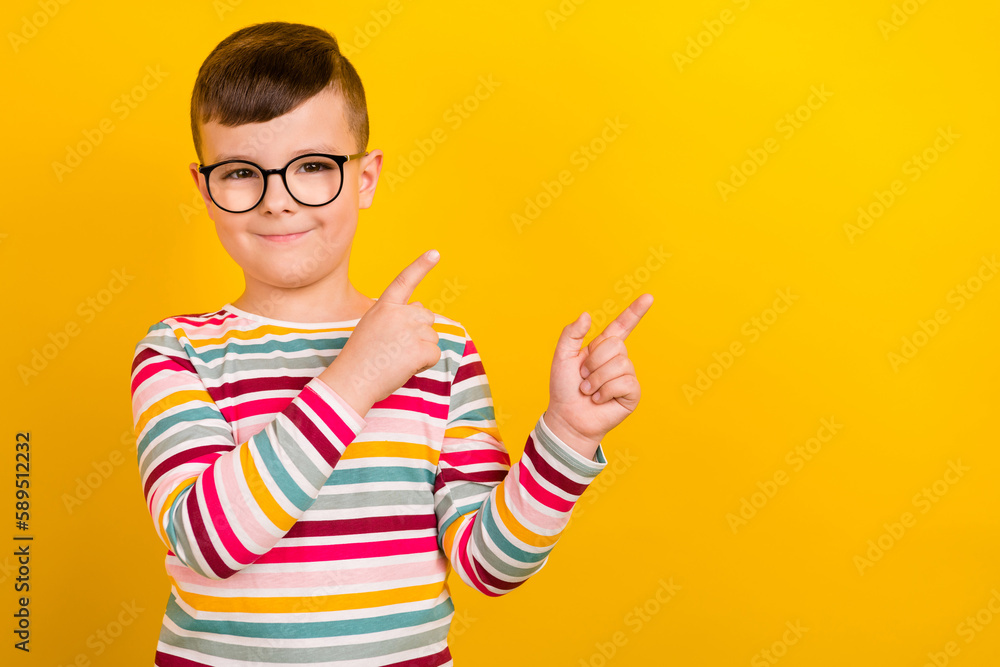 Photo of positive cheerful smart boy wear striped trendy clothes two arm direct empty space cool offers isolated on yellow color background Photo of positive cheerful smart boy wear striped trendy clothes two arm direct empty space cool offers isolated on yellow color background