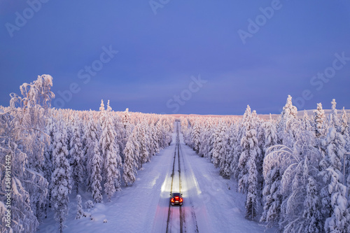 Overhead view of a car driving on empty, icy and slippery road with illuminated headlamps, Akaslompolo, Kolari, Pallas-Yllastunturi National Park, Lapland region, Finland