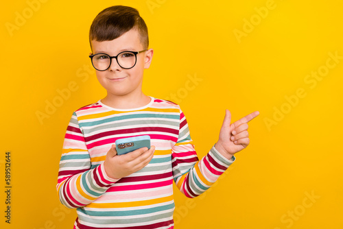 Photo of positive boy user pupil boy wear stylish clothes recommend buy modern device empty space isolated on yellow color background