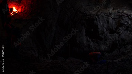 Night excavations in the pit. Archaeologists are excavating artifacts in a deep cave. Bright bonfire and flickering lamplight in a dark underground cave. People are digging the earth in a deep hole
