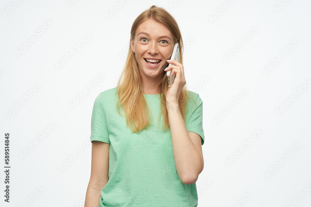 Indoor studio portrait of young ginger female with freckles talking on the phone, isolated over background Indoor studio portrait of young ginger female with freckles talking on the phone, isolated over background