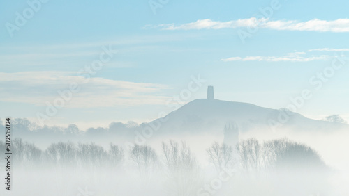 St. Michael's Tower on Glastonbury Tor above the tower of St. John the Baptist's Church on a misty morning in winter, Glastonbury, Somerset photo