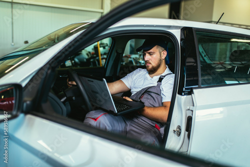 Professional car mechanic working in auto repair service using laptop.