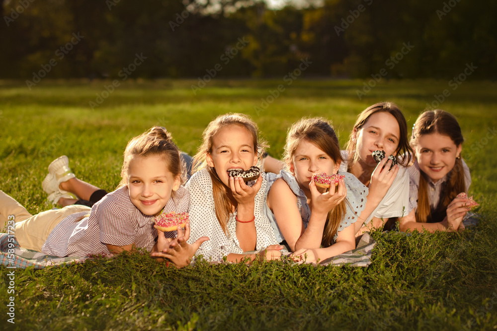 happy children girls eat sweet donuts in green park and have fun in summer camp. Friendship concept happy children girls eat sweet donuts in green park and have fun in summer camp. Friendship concept