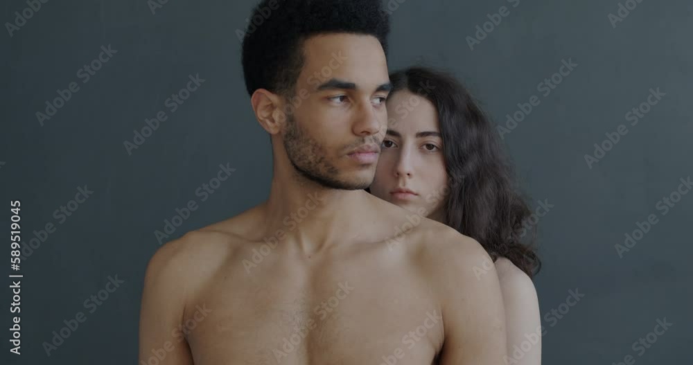 Slow motion portrait of naked couple standing on gray background and looking at camera with serious faces. Expression and relationship concept. Slow motion portrait of naked couple standing on gray background and looking at camera with serious faces. Expression and relationship concept.