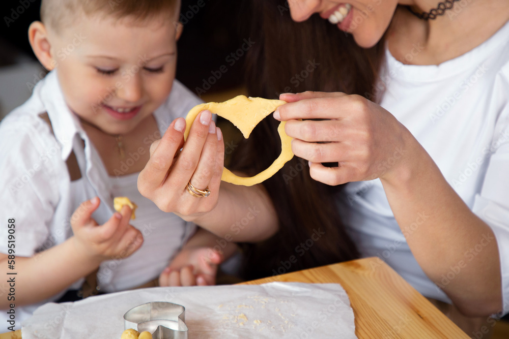 Little boy with his mother preparing heart-shaped cookies in the kitchen, smiling and having fun Little boy with his mother preparing heart-shaped cookies in the kitchen, smiling and having fun