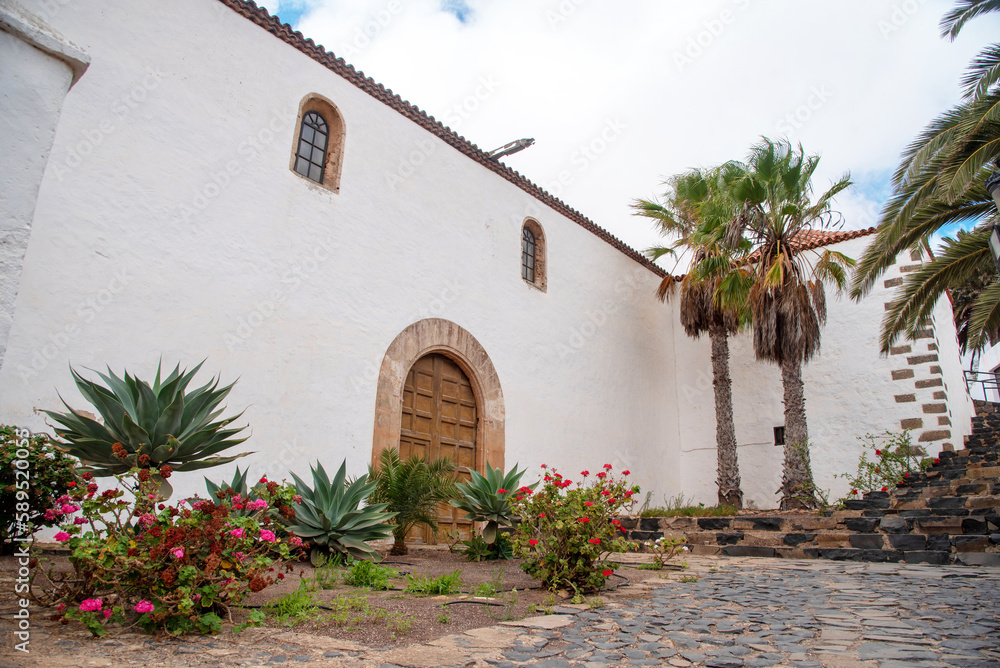 Arquitectura tradicional canaria blanca, edificio con puerta de madera, rodeado de flores y vegetación en el pueblo de Betancuria en Fuerteventura Islas Canarias.