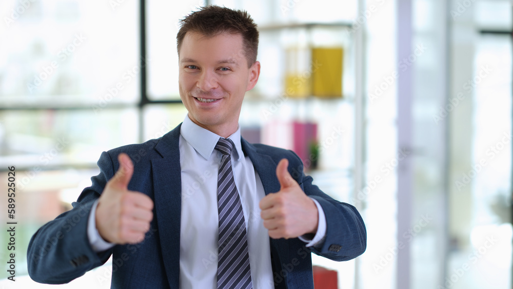 Successful businessman in suit showing thumbs up in office. Success and career growth in business concept Successful businessman in suit showing thumbs up in office. Success and career growth in business concept