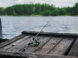 Fishing on the banks of a river or lake, outdoor recreation. Spinning rod reel lies on a wooden pier