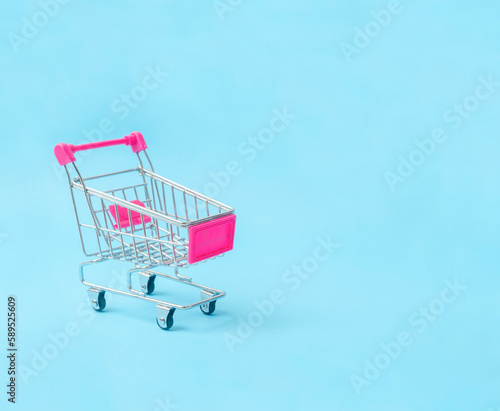 Close-up the empty toy metal supermarket shopping cart on blue background with copy space.