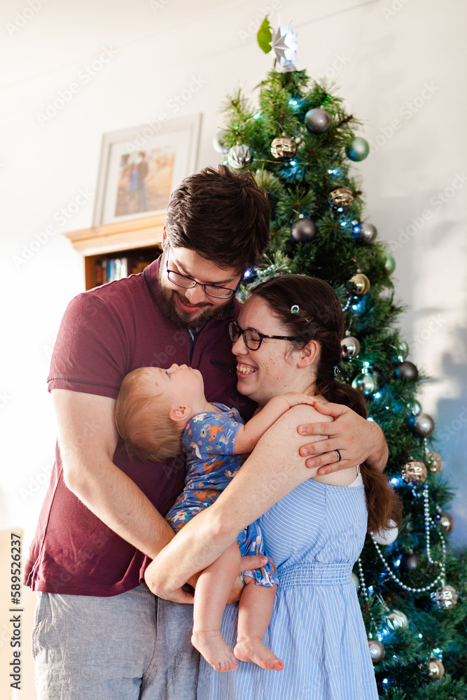 Happy young australian family of three hug beside Christmas tree Happy young australian family of three hug beside Christmas tree