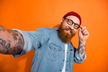 Photo of cheerful young man arm touch glasses make selfie record video isolated on orange color background
