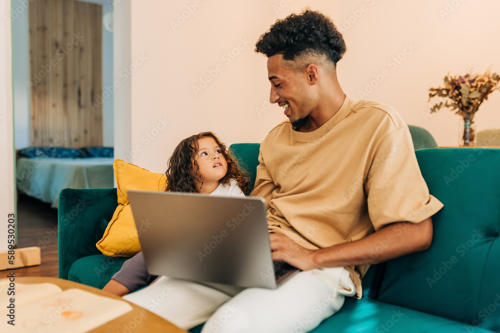 Happy single father using a laptop with his daughter at home Happy single father using a laptop with his daughter at home