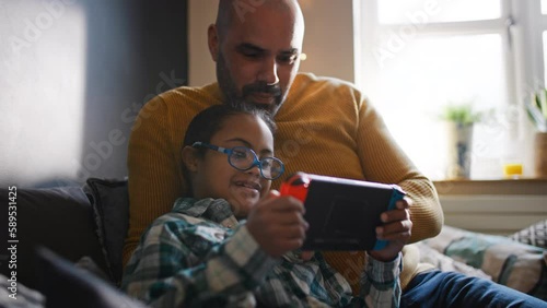 Multiracial father and son with Down syndrome playing computer game