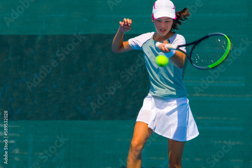 A girl plays tennis on a court with a hard blue surface on a summer sunny day