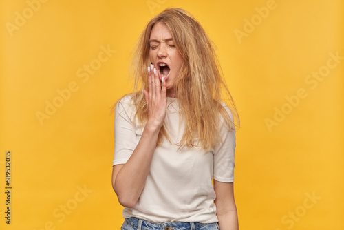 Indoor studio portrait of young ginger female with freckles late on her work, isolated over yellow orange background