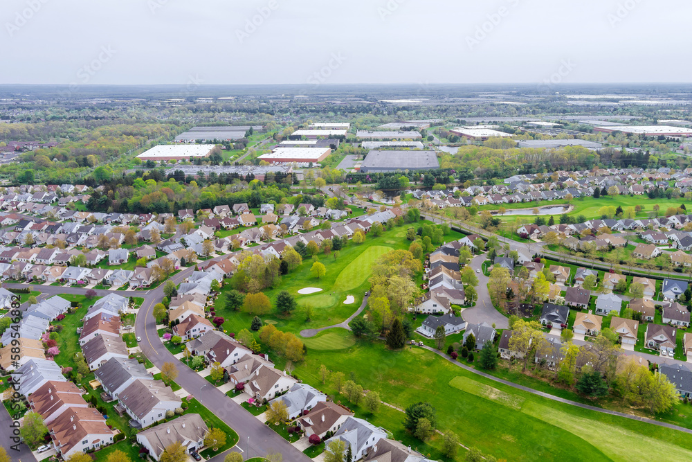 On an aerial panorama view of small American town, there is residential district with houses and roads with spring trees in landscape.