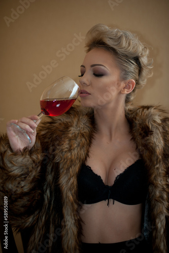 Obraz na płótnie blonde model with pantyhose, glass of red wine ,black bra and fur coat posing provocatively on chair. portrait of sensual blonde, studio shot. Sensual female in black lingerie posing in vintage scene w salonie